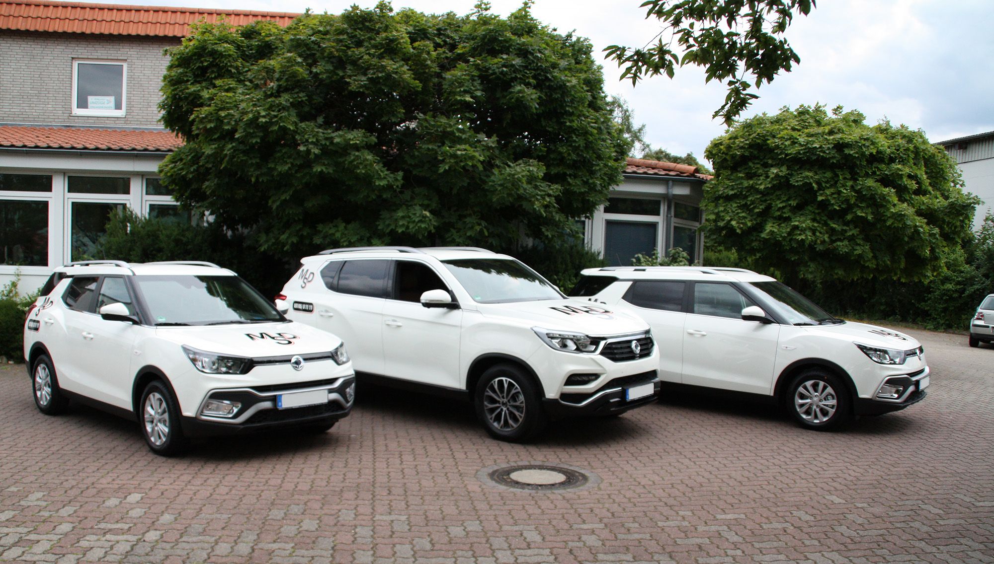 Vor einem Gebäude stehen drei weiße SUVs zum mieten geparkt.